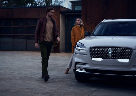 A man and a woman approaching a 2024 Lincoln Aviator® SUV, which illuminates certain lights when they are close | Johnson Sewell Lincoln in Marble Falls TX
